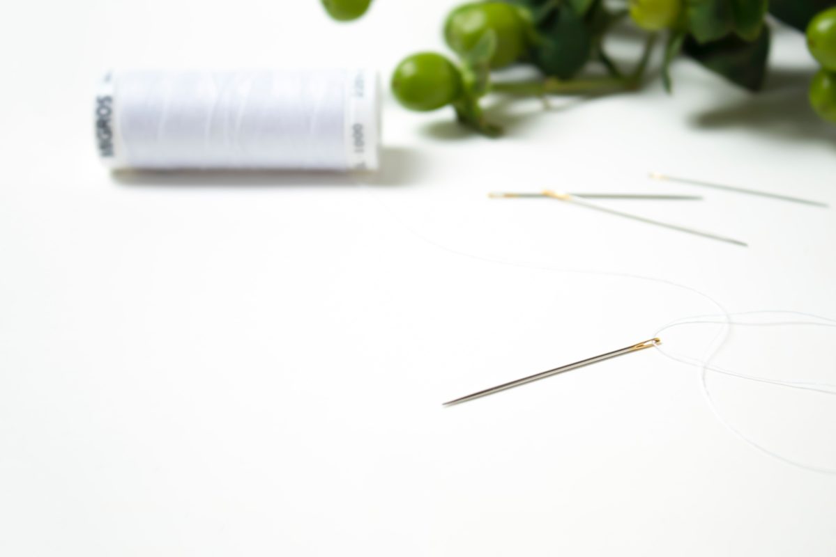 Sewing needles and a white thread bobin on a white table